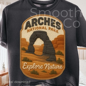 May include: Dark gray t-shirt featuring a detailed graphic of Arches National Park. The design includes the text "Arches National Park" and "Explore Nature" in a vintage style. The graphic showcases the iconic arch formation in a textured, earthy color palette.