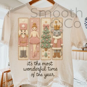 May include: Cream-colored t-shirt featuring a festive design with a nutcracker, ballerina, Christmas tree, and mouse. The design includes the text "it's the most wonderful time of the year". The graphic is in shades of pink, beige, and green.