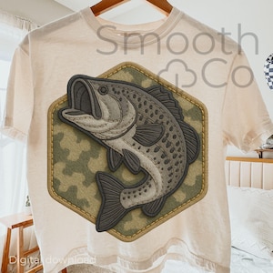 Może przedstawiać: Kremowa koszulka z szczegółową grafiką bassmouth wewnątrz sześciokątnej naszywki. Naszywka ma wzór kamuflażu i szytą obwódkę. Na koszulce widoczny jest napis "Smooth Co".