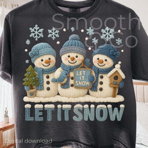 May include: Dark gray t-shirt featuring three snowmen with blue hats, scarves, and carrot noses. The snowmen are holding a bird, a tree, and a birdhouse. The text "LET IT SNOW" is displayed below the snowmen.