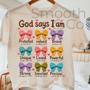 May include: Cream-colored t-shirt with the text "God says I am" in brown. Below are nine colorful crochet bows with words like "Protected," "Valued," and "Brave." Each bow has a corresponding Bible verse.