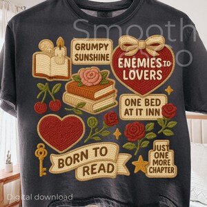 May include: Dark gray t-shirt with a collection of embroidered-style graphics. The design includes a heart, books, roses, cherries, and text that reads "Grumpy Sunshine," "Enemies to Lovers," "Born to Read," and "Just One More Chapter."