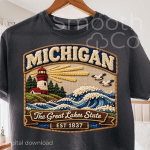 May include: Dark gray t-shirt featuring a detailed embroidered design. The design includes the word "MICHIGAN" above a lighthouse scene with waves, seagulls, and the text "The Great Lakes State EST 1837".