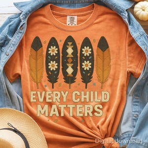 May include: Orange t-shirt with a crew neck featuring a feather design and the text "EVERY CHILD MATTERS" in a tan color. The feathers have a mix of floral and geometric patterns.
