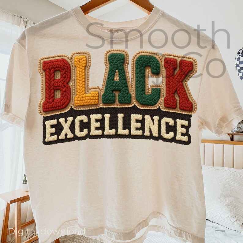 May include: Cream-colored t-shirt with the words "BLACK EXCELLENCE" in a colorful, textured design. The letters are in red, yellow, and green, with a brown border. The shirt is hanging on a wooden hanger.