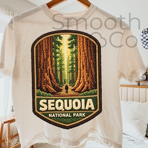 May include: Cream-colored t-shirt featuring a Sequoia National Park design. The graphic shows a path through giant redwood trees, with the words "SEQUOIA NATIONAL PARK" in a green and white banner. The design is framed by a brown border.