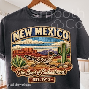 May include: Dark grey t-shirt with an embroidered design. The design features "NEW MEXICO" above a desert scene with a roadrunner, cactus, and the text "The Land of Enchantment - EST. 1912."