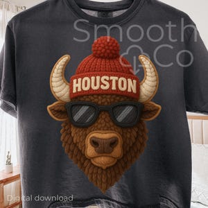 May include: Dark gray t-shirt featuring a detailed illustration of a bison wearing a red knit cap with "HOUSTON" in white letters and black sunglasses. The bison has brown fur and tan horns. The words "Smooth Co" are printed on the shirt.