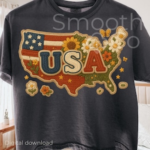 Peut inclure: T-shirt gris foncé avec un motif coloré de la carte des États-Unis. La carte est ornée de fleurs, d'étoiles et du texte "USA". Le motif intègre le drapeau américain et une esthétique rétro.