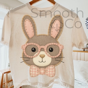 May include: Cream-colored t-shirt featuring a stitched bunny face with pink glasses and a bow tie. The bunny has a gray body, pink ears, and black eyes. The text "Smooth Co" is visible on the shirt.