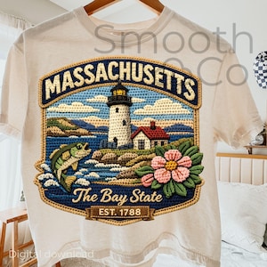 Op de afbeelding: Crèmekleurig T-shirt met een gedetailleerde geborduurde patch. De patch toont een vuurtoren, oceaan en een vis, met de tekst "Massachusetts" en "The Bay State". Het ontwerp bevat een bloem en de tekst "EST. 1788".