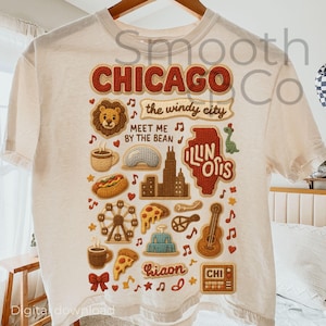 Può includere: T-shirt color crema con grafica a tema Chicago. Il design include la parola "CHICAGO" in un audace font retrò, insieme a illustrazioni di monumenti, cibo e note musicali. È inclusa anche la frase "the windy city".