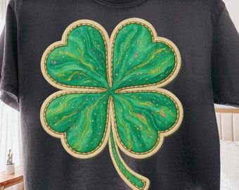 May include: Dark gray t-shirt featuring a large, detailed four-leaf clover design. The clover is a vibrant green with gold accents and a cream-colored border. The words "Digital download" are at the bottom.