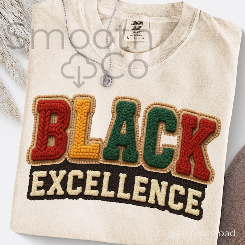 May include: Cream-colored t-shirt with the words "BLACK EXCELLENCE" in a colorful, textured design. The letters are in red, yellow, and green, with a brown border. A silver necklace with a pendant is also visible.