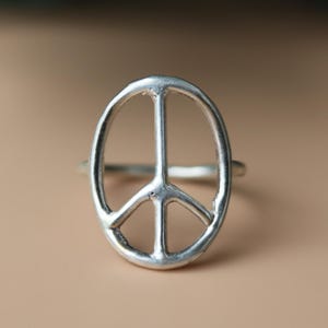 May include: A silver ring with a peace symbol design. The ring has a simple, openwork design with a smooth, polished finish. The peace symbol is centered on the ring's face, with a classic, recognizable shape.