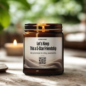 May include: A lit scented candle in a brown glass jar. The label reads "Let's Keep This a 5-Star Friendship" with the promise "We promise to stay awesome." A QR code is also visible. The candle is on a wooden surface.