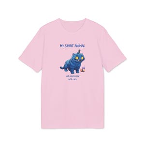 May include: A light pink t-shirt featuring a blue cartoon cat with yellow eyes and a small crown. The text "MY SPIRIT ANIMAL" is above the cat, and "50% PROTECTOR 50% CAOS" is below. The shirt is made of soft material.