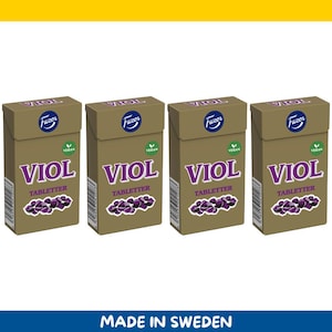 Könnte beinhalten: Vier Schachteln mit VIOL Tabletter, einem veganen Produkt, werden gezeigt. Die Schachteln sind in gedämpftem Braun gehalten und tragen oben den Markennamen Fazer. Das Wort VIOL steht in großen, lila Buchstaben, darunter das Wort TABLETTER. Unten befindet sich ein lila Traubendesign.