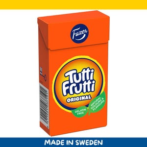Könnte beinhalten: Eine orangefarbene Schachtel mit Tutti Frutti Original Süßigkeiten. Die Schachtel zeigt das Fazer-Logo und ein kreisförmiges Design mit den Worten "Tutti Frutti Original" in Weiß. Die Schachtel weist auch "Gelatinefrei" und "Natürliche Farben & Aromen" auf.