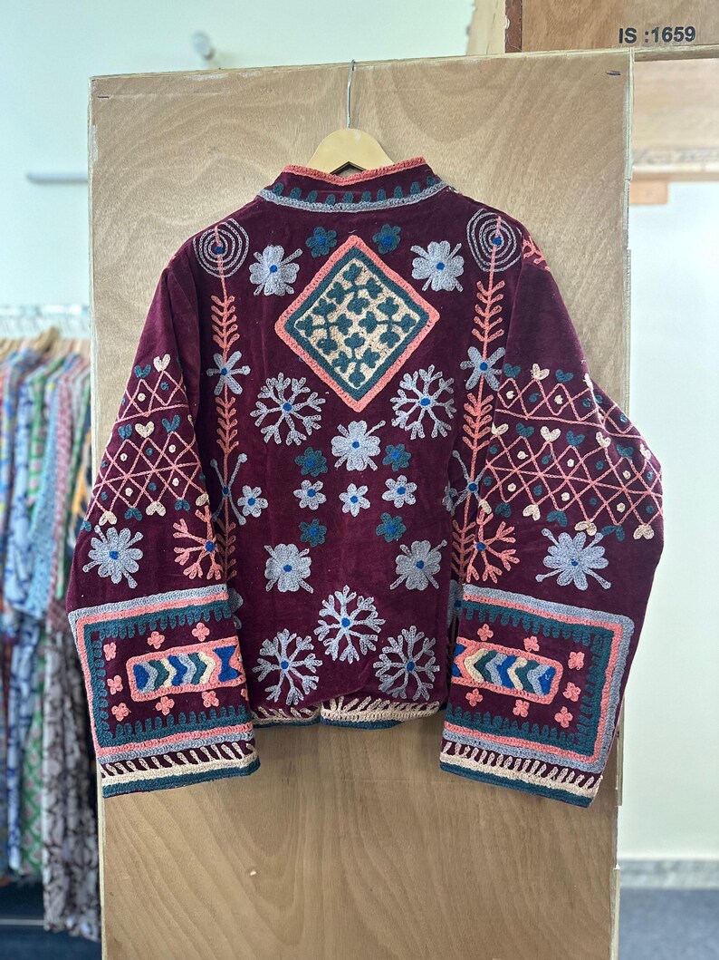 May include: Burgundy jacket with intricate floral and geometric embroidery in shades of pink, blue, and white. The jacket features a high collar and detailed patterns on the sleeves and back, creating a bohemian aesthetic.