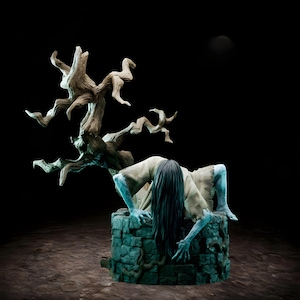 May include: A horror-themed figurine depicts a pale figure with long black hair emerging from a stone well. The figure wears a tattered beige garment and has blue-toned skin. A gnarled tree branch extends above the well against a dark background.