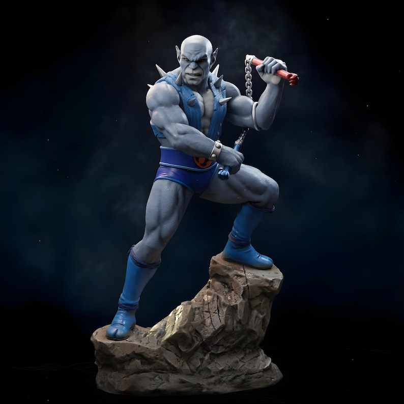 Puede incluir: Estatua detallada de una figura humanoide musculosa de piel gris, posando sobre una base rocosa. La figura lleva pantalones cortos azules, botas y un chaleco con p&uacute;as en los hombros. Sostiene nunchakus rojos y plateados, con expresi&oacute;n decidida.