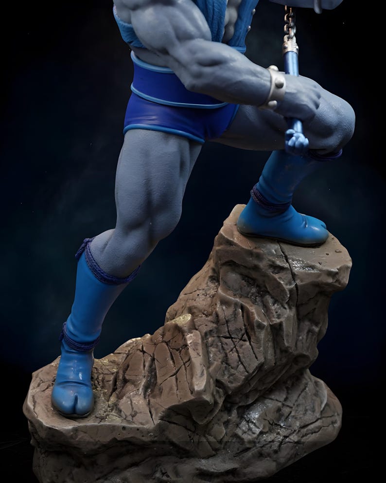 Puede incluir: Estatua detallada de una figura musculosa de piel gris, con pantalones cortos, botas y una parte superior azules. La figura posa sobre una base rocosa, sosteniendo un arma. La estatua tiene detalles intrincados y un fondo oscuro.