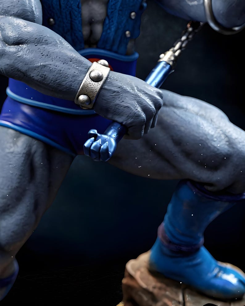 Puede incluir: Primer plano de una figura musculosa de piel gris, con pantalones cortos y botas azules, sosteniendo un arma azul. La figura lleva una pulsera plateada con tachuelas. La imagen est&aacute; sobre un fondo oscuro.