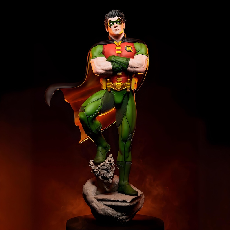 May include: A detailed statue of Robin, a DC Comics superhero, in a dynamic pose. The figure wears a green and red costume with a black cape. The statue is standing on a stone base with a sculpted face. The background is dark with an orange glow.