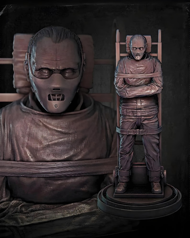 May include: A brown sculpture of a person wearing a mask and restraints, with a second sculpture of a person strapped to a chair. The sculptures are detailed and appear to be based on a movie character.