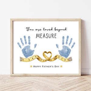 May include: A framed print with the text "You are loved beyond MEASURE" and "HAPPY FATHER'S DAY". It features blue handprints, a yellow tape measure shaped into a heart, and star accents. The print is in a light wood frame.