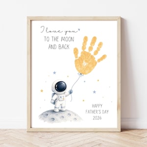 May include: A framed print featuring an astronaut standing on a moon surface, holding a yellow handprint balloon. The text reads I love you TO THE MOON AND BACK and HAPPY FATHER'S DAY 2026, surrounded by small blue and yellow stars on a white background.