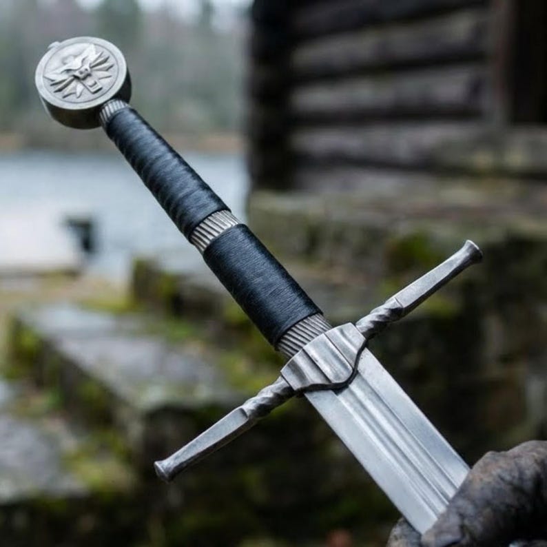 May include: A silver and black sword with a detailed hilt and a blade. The hilt features a circular pommel with a wolf emblem, a black leather-wrapped grip, and a crossguard. The blade is long and sharp, reflecting the light.
