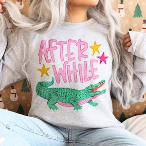 Detailed teal and pink crocodile illustration with "AFTER WHILE" blue hand-lettered graffiti font and green stars, trending boy boutique design for kids' apparel.