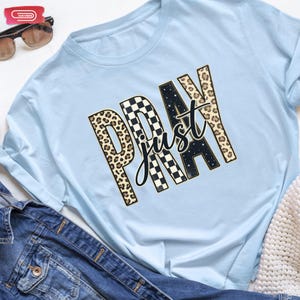Bold "PRAY" text with leopard, checkerboard, and starry patterns, overlaid with a cursive "just" script, featuring a gold outline.