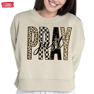 Bold "PRAY" text with leopard, checkerboard, and starry patterns, overlaid with a cursive "just" script, featuring a gold outline.