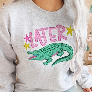 Hand-drawn teal and pink alligator with bold blue graffiti "LATER" text and green stars, boy aesthetic preppy streetwear style for sublimation and DTF.