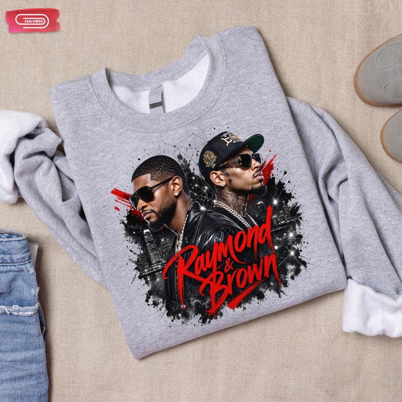 Digital bootleg rap tee graphic featuring R&B artists Usher and Chris Brown standing back-to-back wearing sunglasses and black jackets. The background showcases a high-contrast nighttime city skyline with glowing lights, abstract geometric stars, and bold red brushstroke text reading "Raymond & Brown".