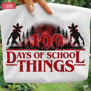Puede incluir: Camiseta blanca con un gráfico rojo. El diseño incluye el texto "100 Days of School Things", siluetas de ciclistas, Demogorgons, una luna roja y un bosque.