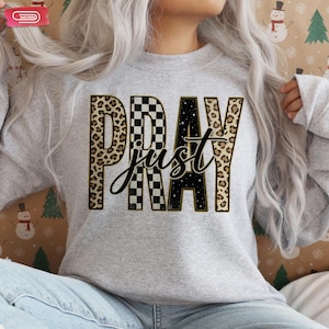 Bold "PRAY" text with leopard, checkerboard, and starry patterns, overlaid with a cursive "just" script, featuring a gold outline.