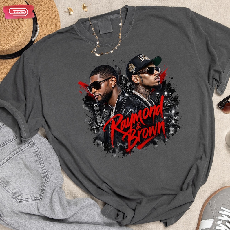 Digital bootleg rap tee graphic featuring R&B artists Usher and Chris Brown standing back-to-back wearing sunglasses and black jackets. The background showcases a high-contrast nighttime city skyline with glowing lights, abstract geometric stars, and bold red brushstroke text reading "Raymond & Brown".