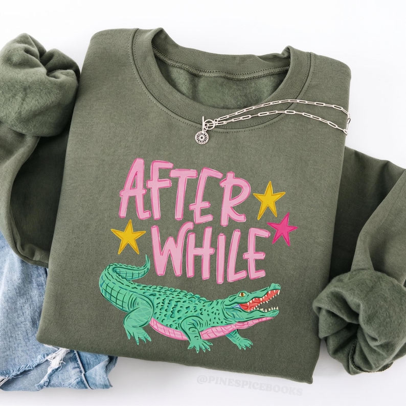 Detailed teal and pink crocodile illustration with "AFTER WHILE" blue hand-lettered graffiti font and green stars, trending boy boutique design for kids' apparel.