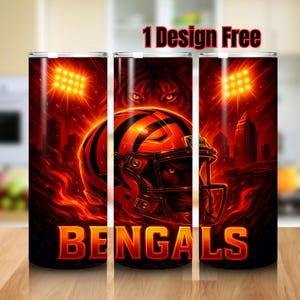 May include: A set of three stainless steel tumblers with a vibrant, fiery design. The design features a football helmet, the word "BENGALS", and a tiger's face, all set against a backdrop of a cityscape and stadium lights. The text "1 Design Free" is at the top.