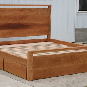 May include: A wooden bed frame with a slatted headboard and footboard. The frame has a storage drawer underneath the bed.