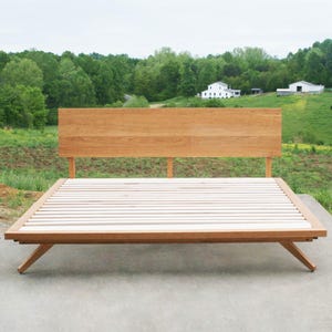 May include: A wooden platform bed frame with a slatted base and a headboard. The bed frame is made of natural wood and has a simple, modern design.