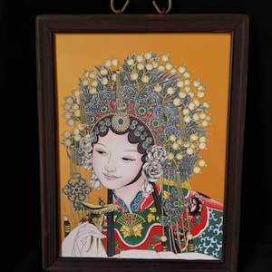 Peut inclure: Une œuvre d'art encadrée représentant une femme en costume d'opéra chinois traditionnel. L'œuvre est dans un cadre en bois brun foncé avec une boucle de suspension en laiton. La femme porte une coiffe ornée de détails floraux et perlés, et un costume coloré.