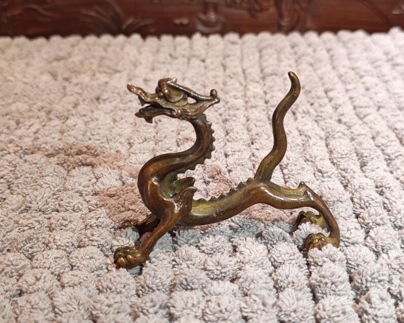 K&ouml;nnte beinhalten: Bronze-farbene Drachenfigur mit aufwendigen Details. Der Drache hat einen langen, geschwungenen K&ouml;rper, vier Beine und einen detaillierten Kopf mit Krone. Die Figur ist aus Metall und ein Dekorationsartikel.