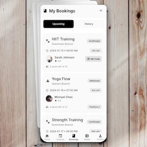 May include: A mobile phone screen displaying a "My Bookings" app interface. The app shows upcoming fitness class bookings, including HIIT Training, Yoga Flow, and Strength Training, with details like time, location, and confirmation status. The background is a light wood grain.