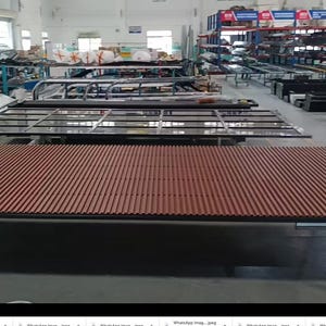 May include: An industrial warehouse scene featuring large, reddish-brown, slatted panels, possibly for construction or architectural use. Several glass-paneled structures and metal frames are also visible, along with shelving units and various materials, suggesting a manufacturing or assembly environment.