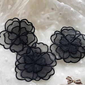Peut inclure: Trois appliques de fleurs gris foncé superposées avec des contours brodés noirs. Les fleurs sont faites d'un tissu transparent, créant une apparence délicate et aérienne. Ces ornements floraux conviennent à divers projets d'artisanat.